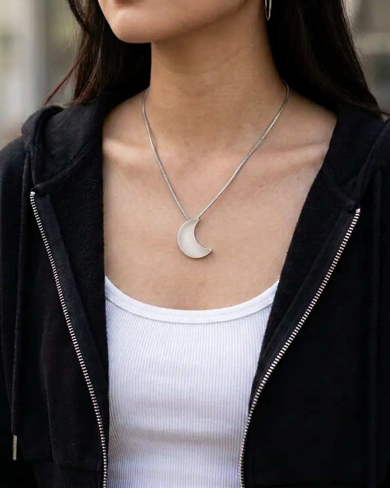 The Moon worn on its chain over a white top and black hoodie.