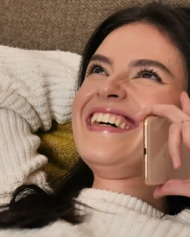 A young woman on a sofa laughing on a phone call