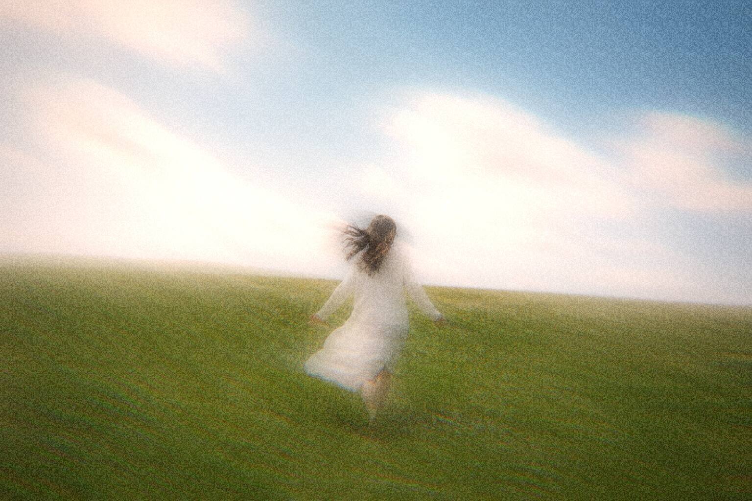 A figure running through an open meadow, motion-blurred under a hazy sky